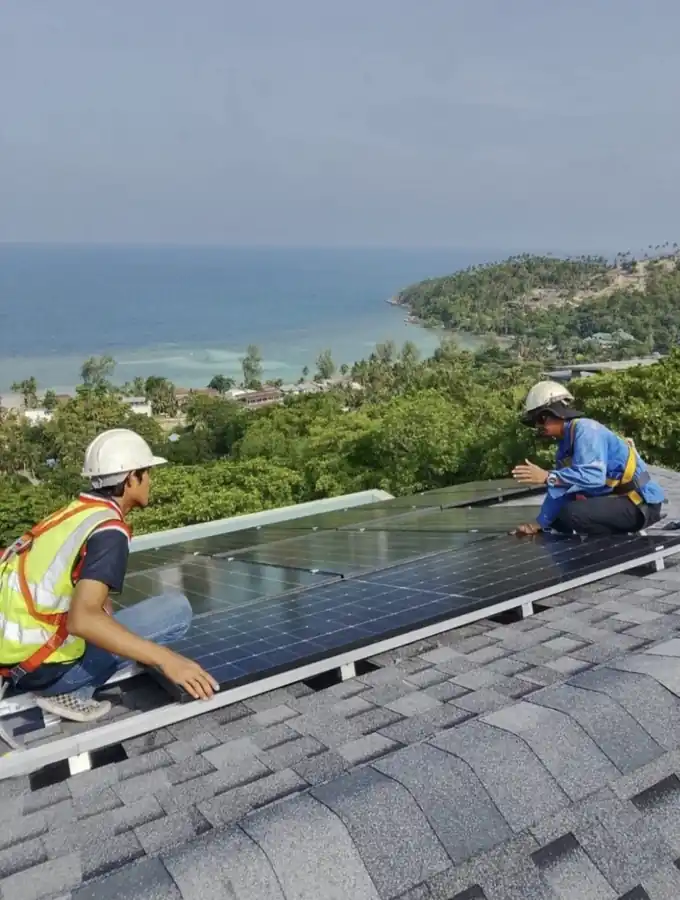 Solar installation technicians fitting rooftop solar panels overlooking the coastline